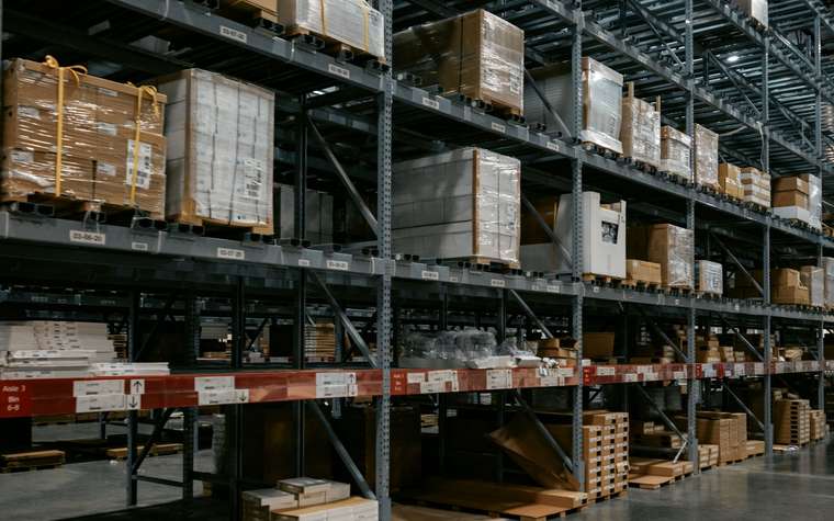 Interior de una bodega con estanterías altas, pallets y cajas