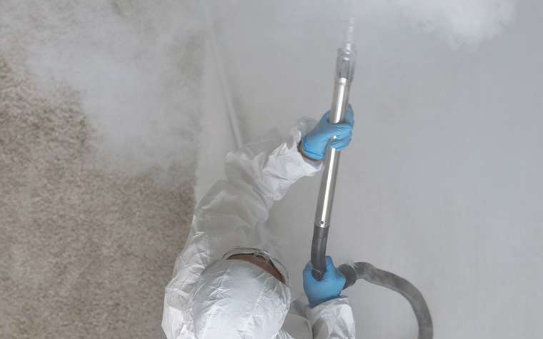 Técnico con guantes y traje protector nebulizando una habitación