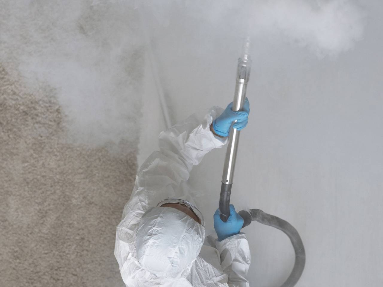 Técnico con guantes y traje protector nebulizando una habitación