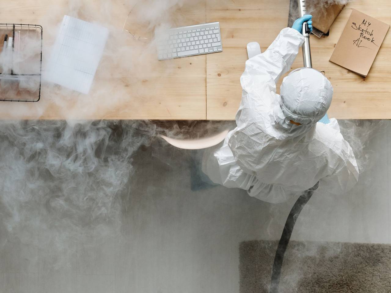 Técnico con traje protector sanitizando un escritorio de oficina con nebulización