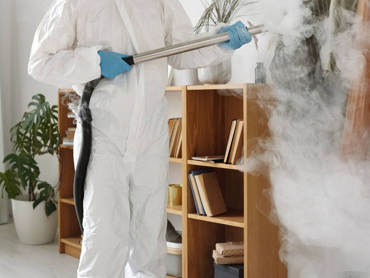 Técnico con traje protector aplicando tratamiento junto a un mueble con libros